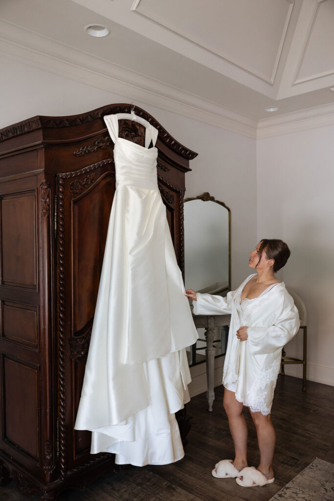 bride admiring her wedding gown hanging up on armoire
