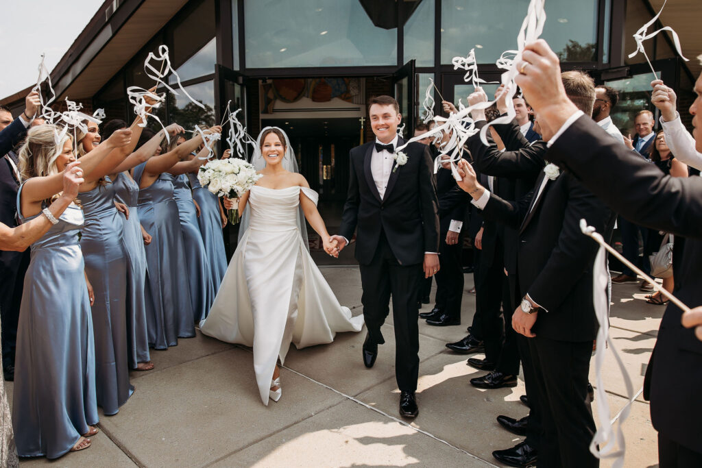 bride and groom recess out of church while guests wave ribbons